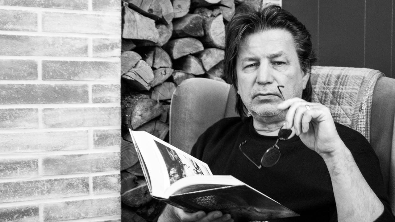 Man reading a book by a fireplace.